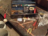 Wide shot showing metal toolbox and assortment of hand tools including pliers, hammer, screwdrivers, scissors, socket bits.