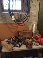 Image of various bungee cords, electrical cords, cable snakes, tools on a white table beneath a basement window.
