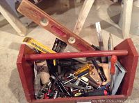 Top view of wooden toolbox filled with assorted hand tools and hardware, showing screwdriver handles and level