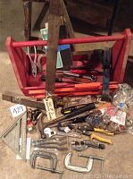 Photo of the wooden toolbox with various hand tools arranged in front and inside it, including saw, clamps, pliers, and brushes.