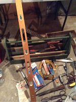 Overview of assorted hand tools and green wooden toolbox including level, pliers, saws, clamp, hammer, and coiled wire.