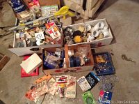 Photo showing boxes containing mixed new hardware parts including pipe fittings, small tools, and packaging with various small hardware components.