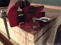Full view of the red Fuller 3.5 inch bench vise mounted on a wooden workbench showing handle and jaw assembly.