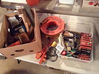 Photo showing a box of wire brushes, orange electrical extension cord, and other assorted hardware laid out on a surface.