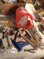 Wide view of assortment of hand tools on floor with orange bucket containing plastic wrap or insulation sleeves and additional tools