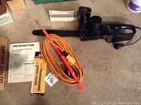 Remington 14-inch electric chain saw, orange extension cord, operator's manual, and replacement chain/parts box arranged on concrete floor.