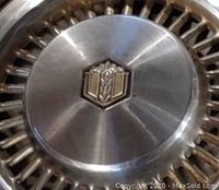 Close-up of the central emblem on one vintage hubcap showing a shield with gold accents and grain motif.