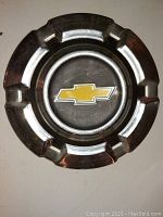 Single vintage Chevrolet hubcap showing front detail with yellow bowtie emblem and polished metal finish.