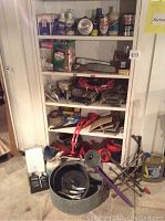 Full view of white metal cabinet containing various automotive supplies and tools, with some items placed on the ground in front of it.