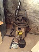 Full view of Shop-Vac with hose coiled around handle and accessories on floor in front.