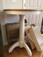 Full view of bar-height wooden pedestal table showing round wooden top with light colored base and legs.