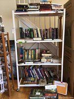 White metal shelving unit with three shelves filled with hardback books and a box of autographed photos.