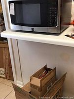 Kenmore microwave on countertop with cardboard boxes below and part of white counter visible.