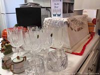 Photo showing five cut crystal stemmed goblets, ceramic creamer and sugar, glass lidded pot, and part of the wooden bread box with lace doily on top.