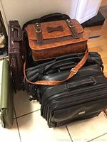 Photo of five briefcases and travel bag arranged on floor showing variety of leather and styles.