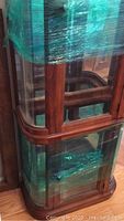 Curio cabinet partially wrapped in plastic showing glass panels and wood finish.