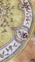 Close-up photo of the front pattern of the rug showing floral and ornate border design in gold, cream, pink, blue, and green tones on thick pile.