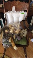 Wide view showing dark oak rocking chair with carved back and green seat cushion holding multiple plush bears, some wrapped in plastic bags.
