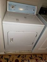 Photo of the Kenmore electric dryer showing its front door, white exterior, and placement between other appliances.