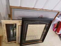View of multiple framed wall art pieces stacked leaning against a wall, including the Declaration of Independence print, Latin study print, and other framed art pieces with various frames.