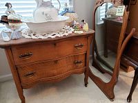 Full view of the antique wooden dresser with matching framed mirror positioned beside it. Decorative figurines and a ceramic basin arranged on top of the dresser.