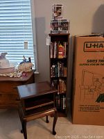 Telephone table, swivel bookcase filled with books, and a large U-Haul box in background.