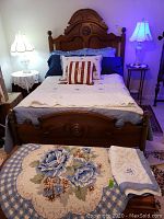Full view of vintage half full wooden bed frame dressed with bedding and illuminated by table lamps, showing headboard, bedspread, pillows and throw rug on floor