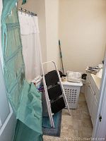 Green hanging shoe organizer with clear plastic pockets and white/black step ladder and laundry hamper visible behind