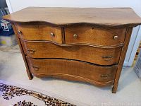 Front view showing dresser with five drawers, two small on top with brass knobs, three larger below with brass drop handles, curved front.
