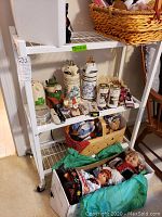First shelving unit shown loaded with decorative ceramic canisters and dolls in a box on the lower shelf