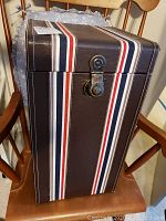 Closed view of the vintage-style trunk with striped cover and metal latch on a wooden chair.