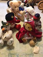 Photo shows several collectible plush bears and a baby bunny arranged on carpet. Includes bears dressed as Little Red Riding Hood, Bavarian Snowman, Braves baseball players, and others.