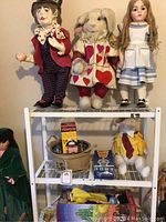 Shelf top row: Mad Hatter doll, White Rabbit plush in card suit costume, porcelain Alice doll