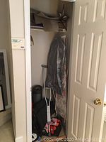 Closet showing hanging garment bags, metal crutches, red first aid kit, and foldable wagon partially visible.