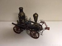 Side angle view of metal steam vehicle showing detailed boiler, chimney, and mechanical components with reddish spoked wheels.