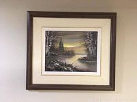 Framed oil painting showing a landscape with trees and a lake or river under a twilight sky.