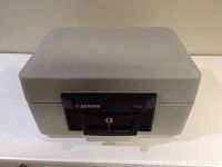 Closed view of the Sentry 1150 portable fire safe showing grey exterior with black locking handle and keyhole.