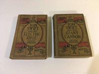 Two Tom Swift books with illustrated front covers showing 'Tom Swift and His Electric Rifle' and 'Tom Swift and His Giant Cannon'. Both books have tan cloth covers and feature colorful vintage-style illustrations.