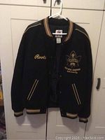 Front view of black Roots bomber jacket with embroidered maple leaf and gold medal champions design