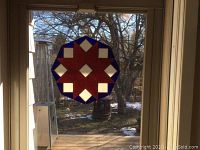 Round stained glass panel hung by a chain against a window, showing outdoor background. Visible small crack near center but panel appears solid.