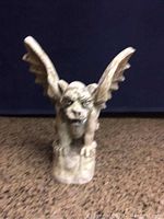 Front view of a solid concrete gargoyle statue showing details of the face and wings.