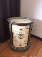 Front view of one oval end table showing three closed drawers with painted floral design