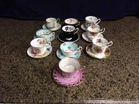 Photo showing ten assorted floral tea cups with matching saucers arranged on countertop.