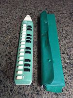 Full view of green Hohner melodica soprano and matching green textured carrying case side by side on a granite surface.