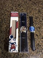 Two Disney wristwatches shown; one watch in original Disney Parks box unopened, the other outside packaging.