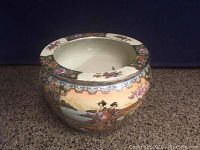 Full view of round oriental ceramic bowl featuring painted Asian scenery and floral designs on exterior surface and rim.