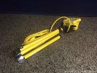 Folded view of yellow halogen light on tripod stand with cord wrapped around legs. Showing compact size and folded configuration.