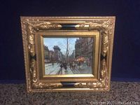 Frontal view of the framed oil painting showing street scene with pedestrians and buildings.
