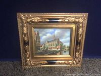 Frontal view of the painting in ornate gold frame showing detailed European architectural scene with a church, canal, and surrounding buildings under blue sky with clouds.