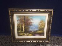 Full view of the framed painting showing forest scene with birch trees and pathway, gold frame and white matting.